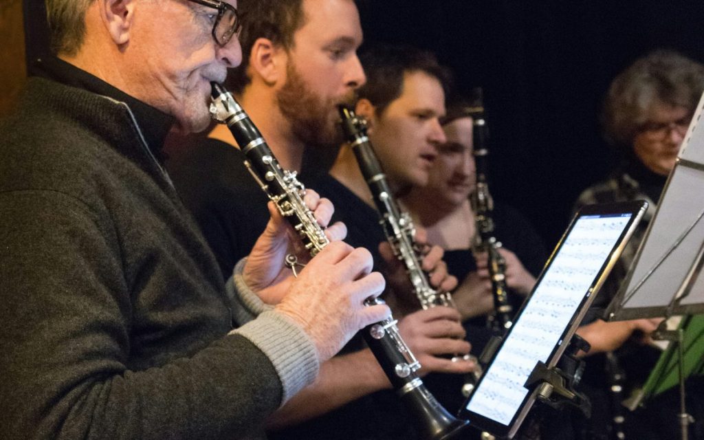 Adult clarinet section playing from sheet music in a community concert band