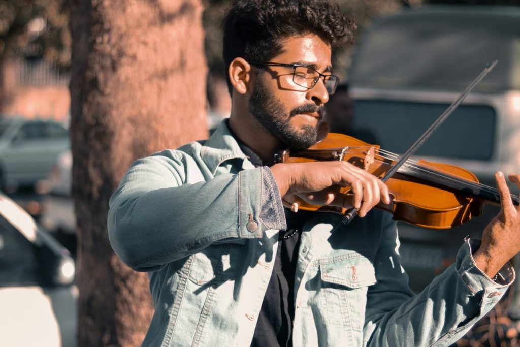 Young fiddler in glasses playing the fiddle outdoors